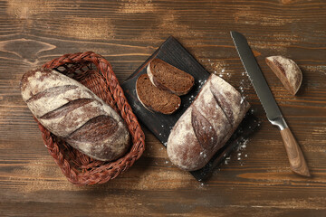 Board with cut loaf of fresh rye bread and knife on wooden table