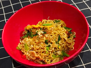 A bright red bowl filled with delicious fried noodles with sliced ​​egg, mustard greens, crispy...