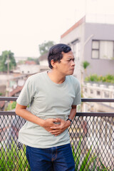 A man experiencing stomach pain on a balcony with an urban backdrop showcasing discomfort