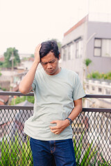 Worried man on a balcony looking down, head in hand, stomach ache, urban scene, outdoor setting