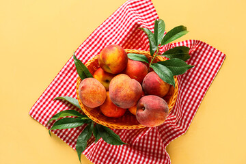 Wicker basket of fresh peaches on yellow background, top view