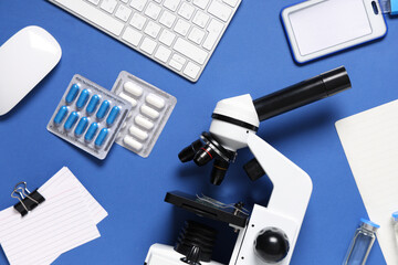 Modern microscope with different medicine, notebooks and keyboard on blue background