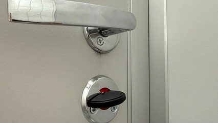 Close-up of a metal door handle and lock on a public restroom stall door, showing the privacy...