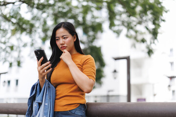 Pensive young woman reading a message on her smartphone in a city park
