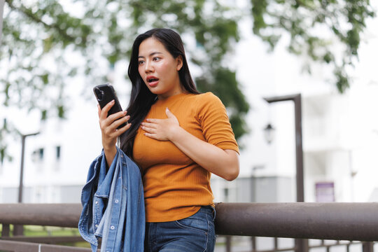 Shocked young woman reading bad news on smartphone outdoors