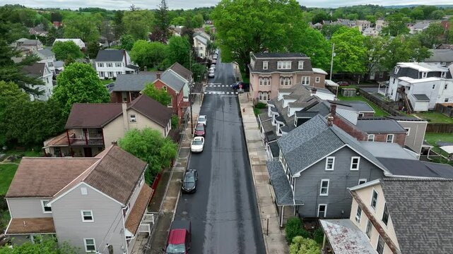 Black car crossing junction of quiet american neighborhood with row of houses in classical style. Geren trees in spring. American city neighborhood with townhouses and historic row homes.