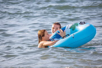 A cheerful young couple swims in the sea with an inflatable circle
