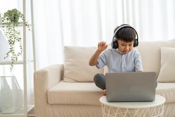 Naklejka premium Asian boy using laptop with headphones course online learning, distance education for kids, e-learning at home, child studying digital technology, interactive education platform, remote class tutorial
