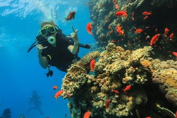 Scuba diver underwater making OK hand sign near vibrant coral reef with colorful tropical fish....