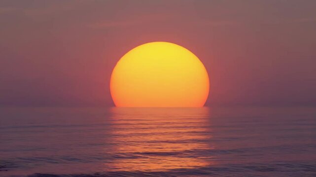 Large orange sun setting over calm ocean water.