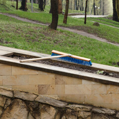 Blue brush on wooden handle lying on stone planter wall in park setting