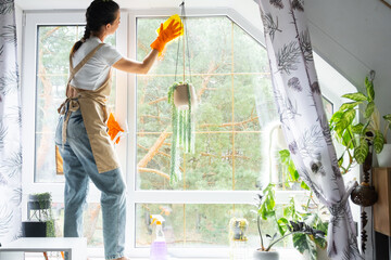Woman in rubber gloves and apron manually washes attic window of house with rag cleaner and mop...