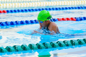 Swimmer child swims breaststroke swimming style in a race swimming pool. Water sports and...