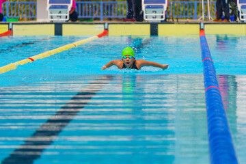 Swimmer child swims butterfly swimming style in a race swimming pool. Water sports and competition,...