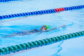 Swimmer child swims backstroke swimming style in a race swimming pool. Water sports and...