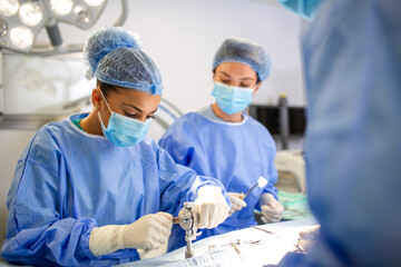 Female surgeon using orthopedic surgical equipment during a medical procedure. Concentrated and...
