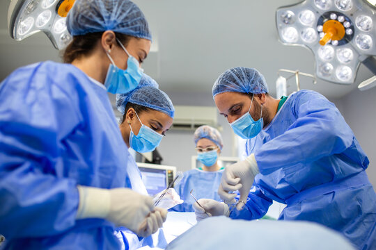 Medical team performing a surgical procedure in a modern operating room. Surgeons in blue scrubs and masks are focused on the operation with equipment in the background. - Powered by Adobe