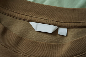 Close up of blank white clothing care label on shirt fabric background.