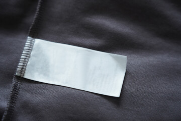 Close up of blank white clothing care label on black shirt fabric background.