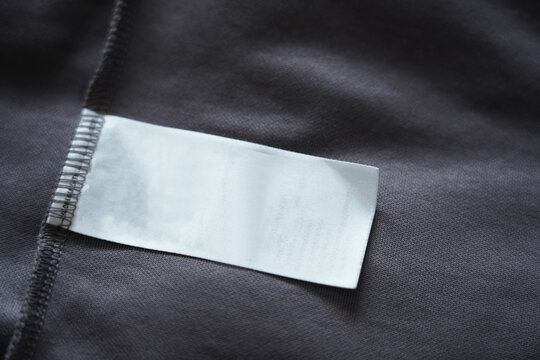 Close up of blank white clothing care label on black shirt fabric background.
