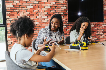 Young girls engage in a hands-on robotics activity with a teacher guiding them. They assemble and operate robot arms in a classroom, fostering creativity, problem-solving, and STEM education skills.