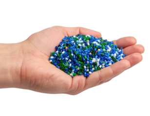 A hand holding a pile of small colorful plastic pellets in blue, green, white, and turquoise shades.