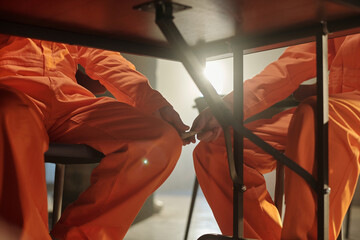 Two men in orange prison uniforms sitting at table in prison library, one man passing small item to inmate