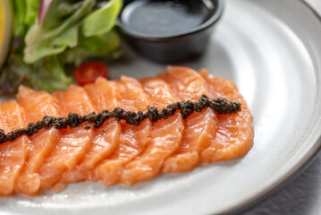 Fresh salmon sashimi with caviar and salad on a white plate.