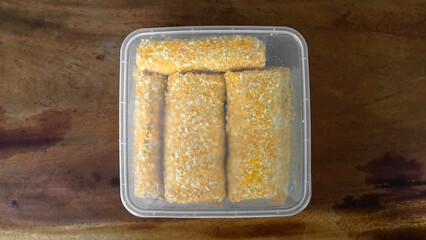 Jakarta, 30 June 2025 : Frozen breaded spring rolls with kaffir lime leaves on wooden background....