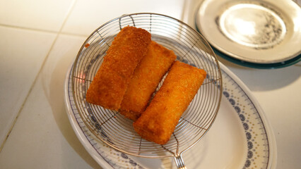Jakarta, 30 June 2025 : Frozen breaded spring rolls with kaffir lime leaves on wooden background....