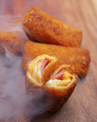 Jakarta, 30 June 2025 : Frozen breaded spring rolls with kaffir lime leaves on wooden background. Raw snack food ready to cook