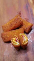 Jakarta, 30 June 2025 : Frozen breaded spring rolls with kaffir lime leaves on wooden background. Raw snack food ready to cook