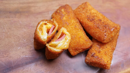 Jakarta, 30 June 2025 : Frozen breaded spring rolls with kaffir lime leaves on wooden background. Raw snack food ready to cook