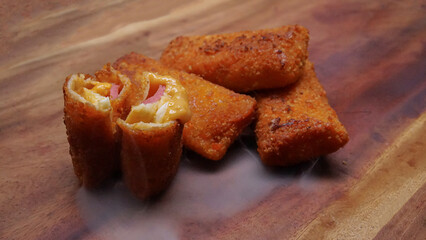 Jakarta, 30 June 2025 : Frozen breaded spring rolls with kaffir lime leaves on wooden background. Raw snack food ready to cook