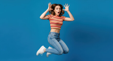 Obraz premium A young woman jumps with surprise against a vibrant blue background