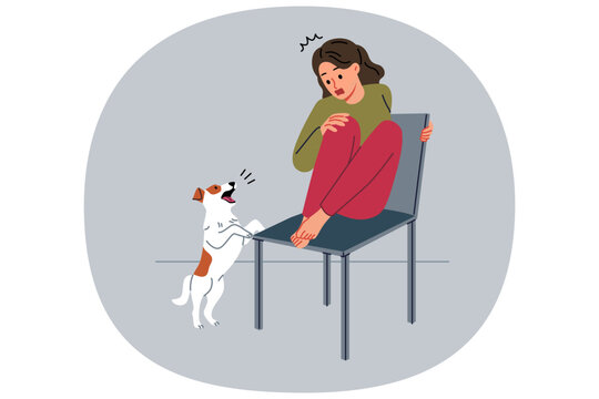 Teenage girl is afraid of dog and climbs onto chair to hide from puppy and needs treatment for cynophobia. Kid feels panic attack at sight of pets due to cynophobia or possibility of allergic reaction