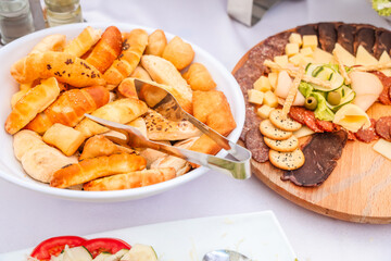 Assorted pastry bread, deli meats, cheese cubes and crackers served on a catering table, perfect for breakfast buffet or festive appetizer arrangement.