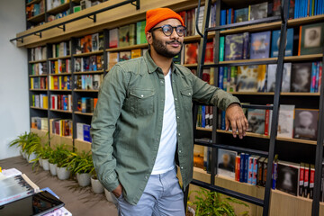 Bearded young man in an orange hat standing near the book shelf
