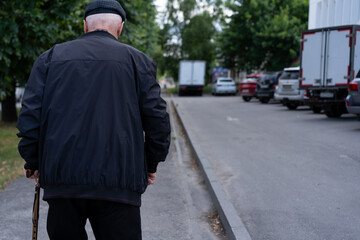 Elderly man walking in a quiet street lined with parked cars in a peaceful neighborhood during...