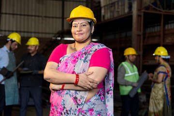 Portrait of beautiful young woman in hardhat confidently at camera enjoying work in modern factory