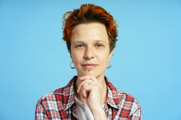 Portrait of redhead bigender person with facial piercing looking at camera on blue backdrop