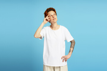 Young woman with tattoo and piercing posing in studio, looking to side, isolated on blue