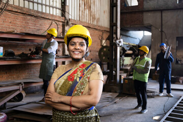 Portrait of beautiful young woman in hardhat confidently at camera enjoying work in modern factory