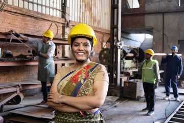 Portrait of beautiful young woman in hardhat confidently at camera enjoying work in modern factory