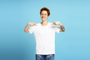 Portrait of stylish woman with piercing and tattoo pointing fingers to white t shirt in studio