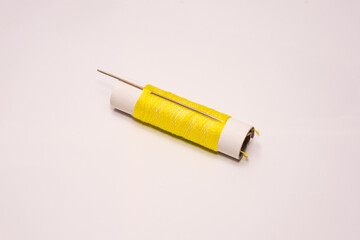 A macro shot of a vintage spool wrapped with yellow thread, paired with an aged sewing needle, resting on a clean white background. Ideal for sewing, DIY, or handmade concept visuals.