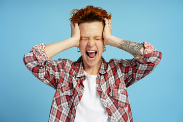 Emotional woman with closed eyes touching her face head and screaming, isolated on blue