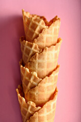 Crisp waffle cones are neatly stacked, awaiting delicious ice cream filling, all set against a vibrant pink background