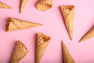 Waffle cones of varying orientations lie on a soft pink background, awaiting the perfect ice cream scoop to fill them with flavor