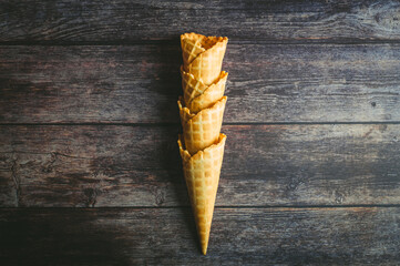Four waffle cones are arranged vertically on a rustic wooden background, inviting ice cream lovers...